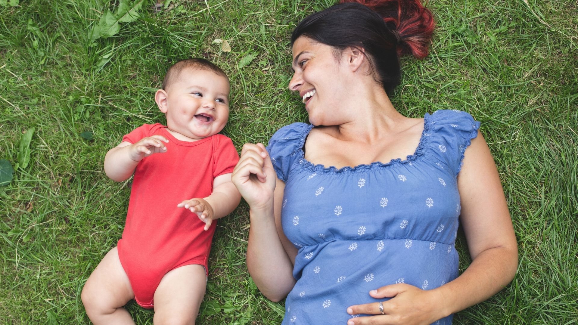 Mother and her baby laughing and laying on the grass outdoors