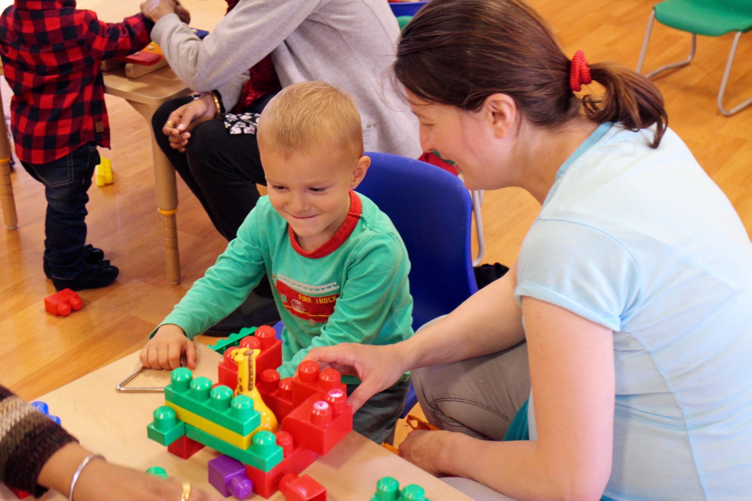 Early years practitioner helping a child play with building blocks, in the classroom