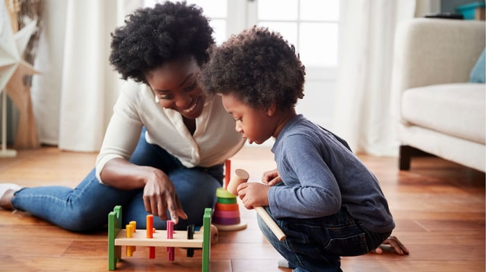 Mum and child sitting on the floor playing with a wooden toy