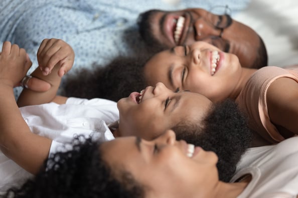 Mum and dad laying in bed, in different directions beside their toddlers