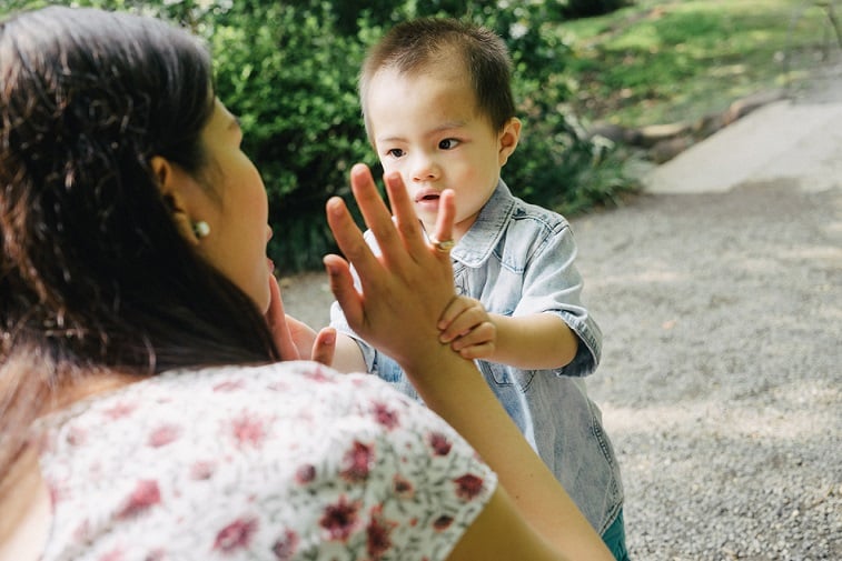 Mum crouching on the ground outdoors, holding one hand up near her face, while talking to her baby