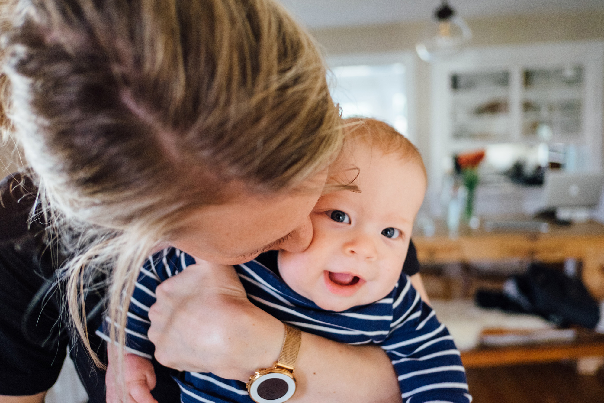 Mum holding their baby from behind and giving him a kiss on his cheek