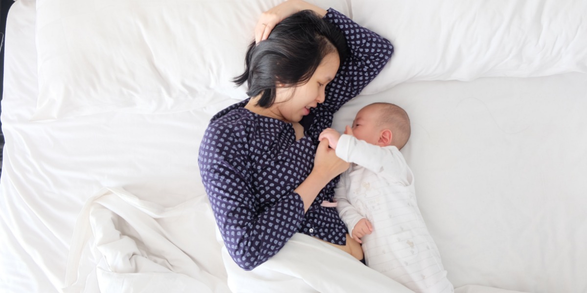 Mother wearing a navy top comforting her baby in bed before bedtime