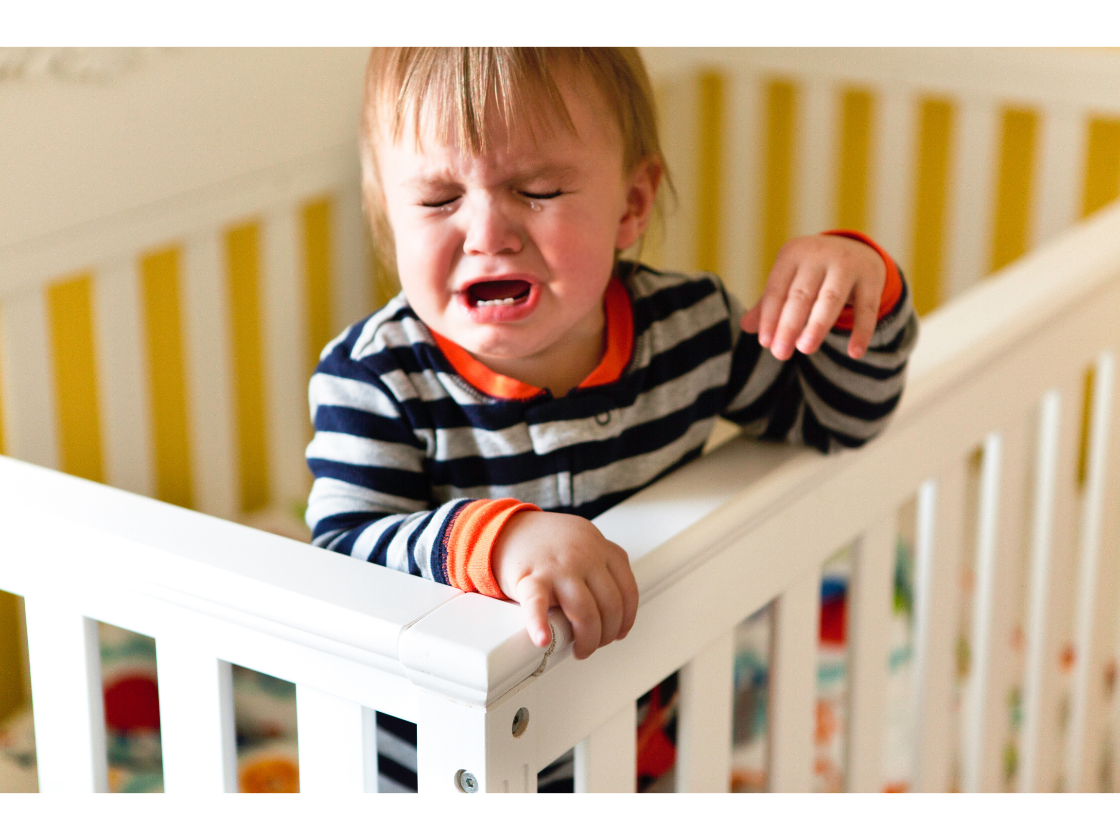 Toddler holding onto the edge of his cot, while throwing a tantrum