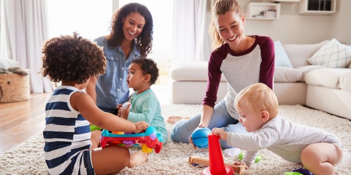 Two mothers sitting on the carpet, playing with their children in the living room