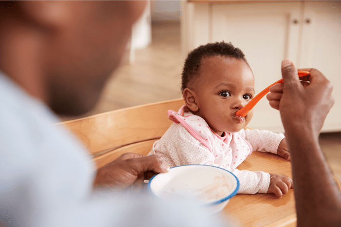 Baby eating food from a spoon while being fed