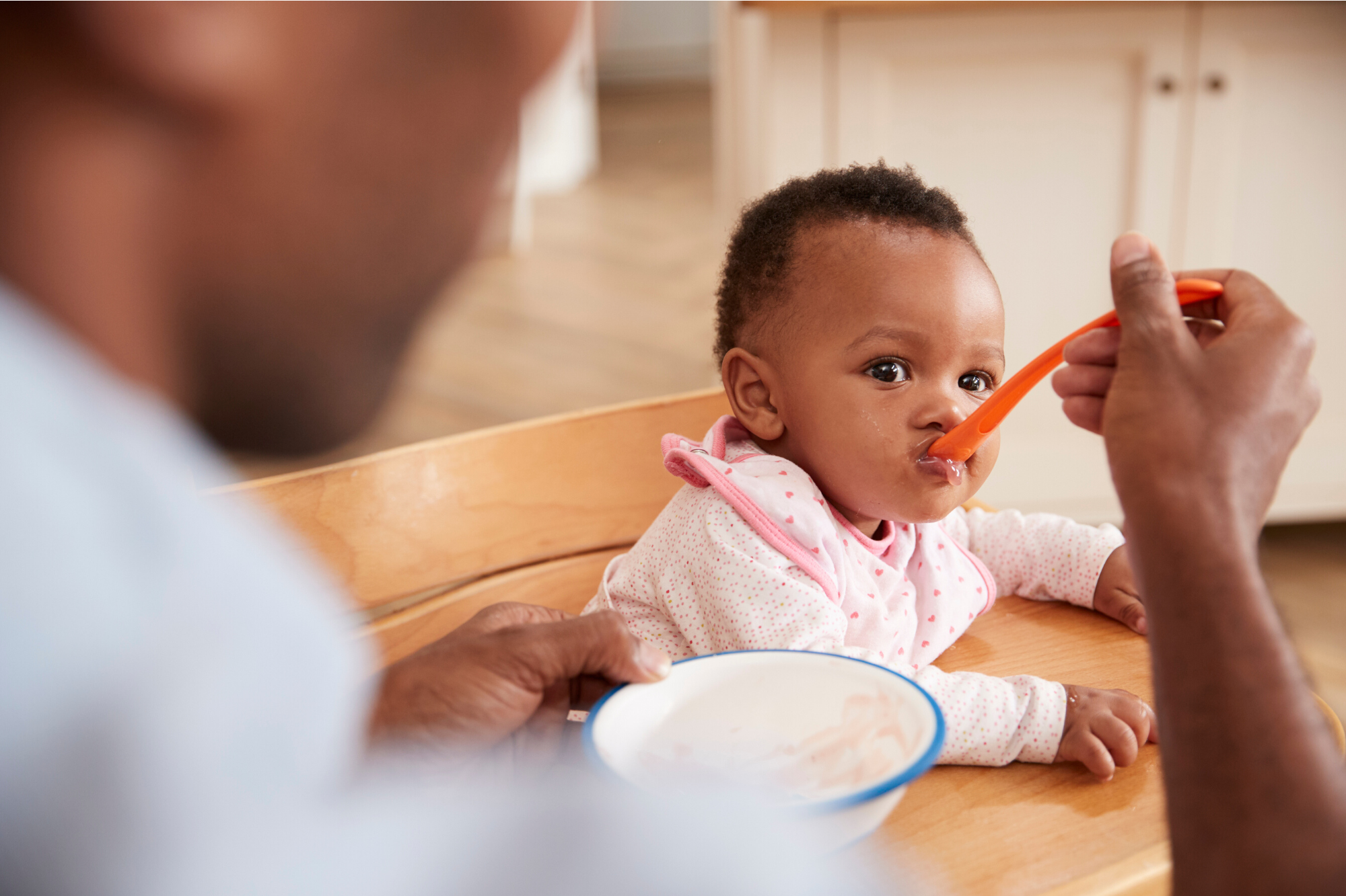 Baby eating food from a spoon while being fed