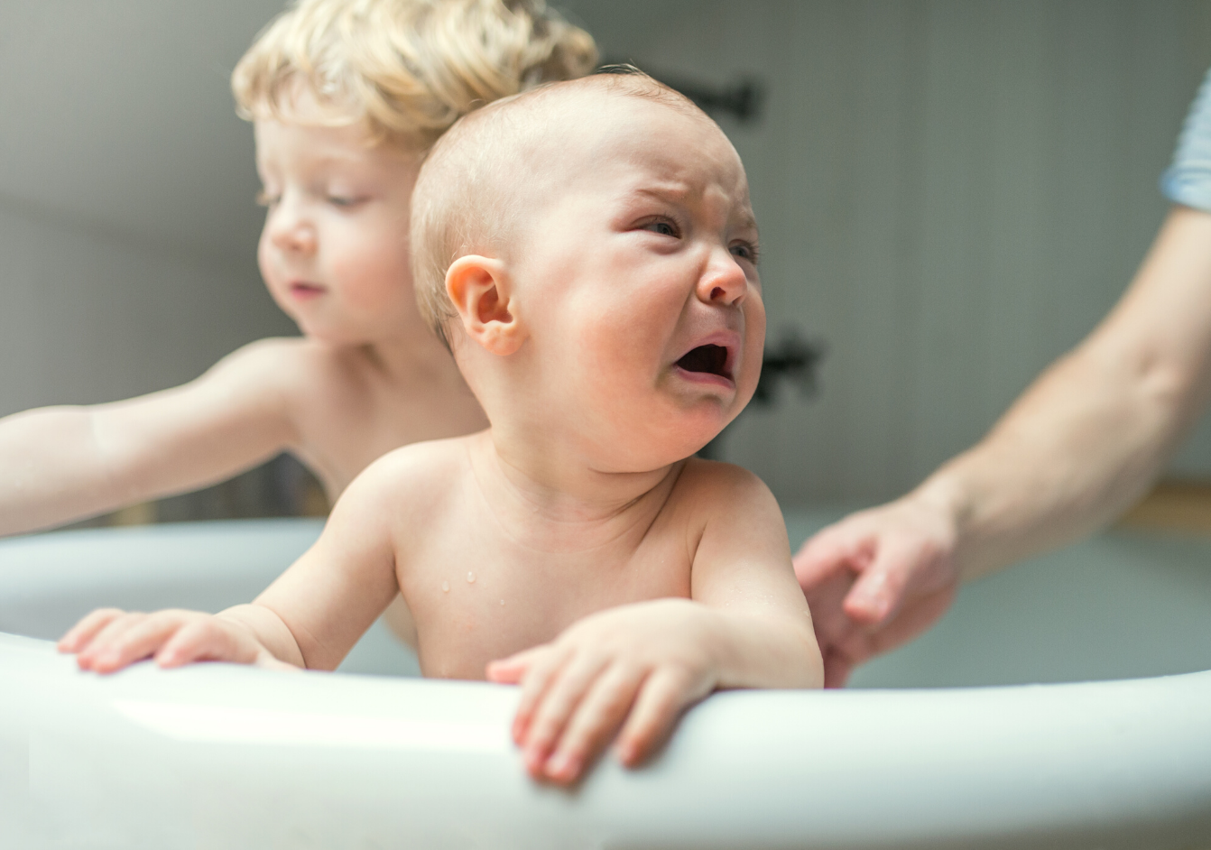 two babies in a bath, one baby is having a tantrum