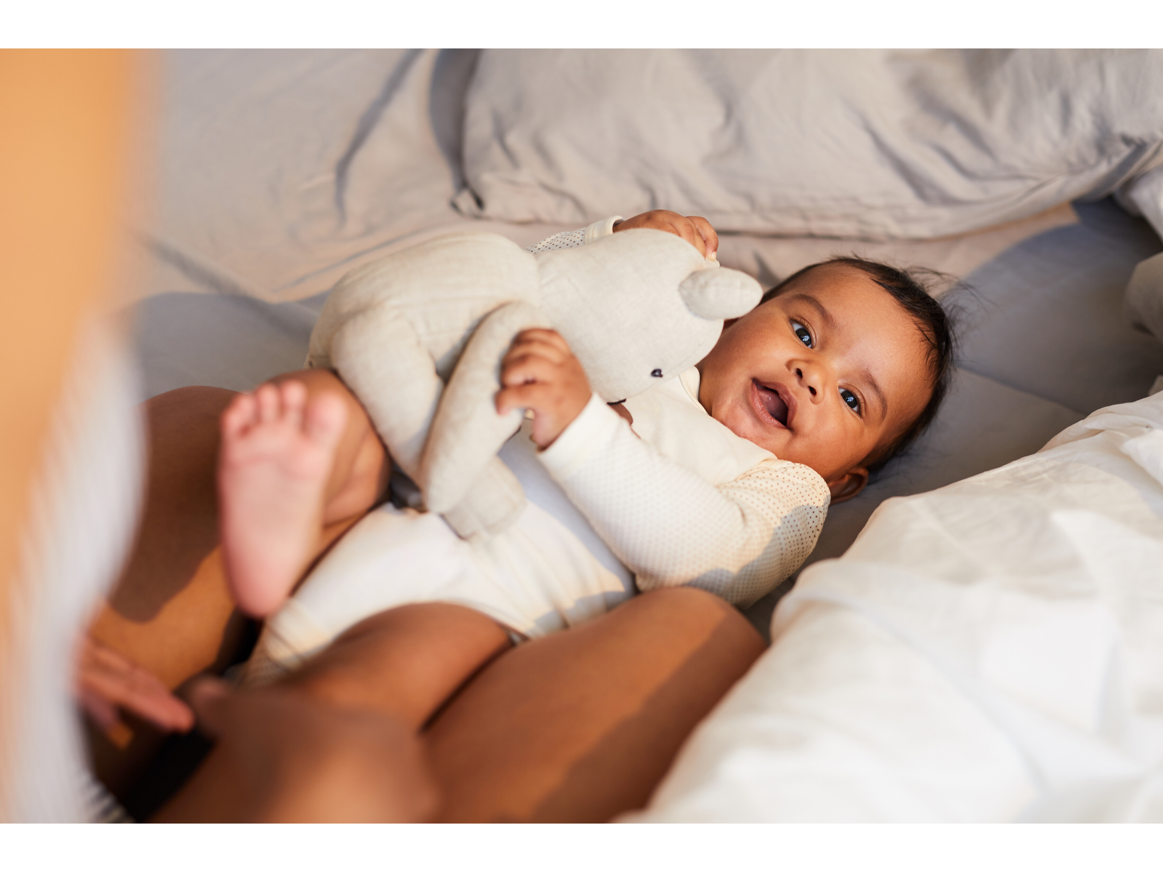 Happy baby after a good sleep, wearings a white onesie and cuddling her white teddy bear