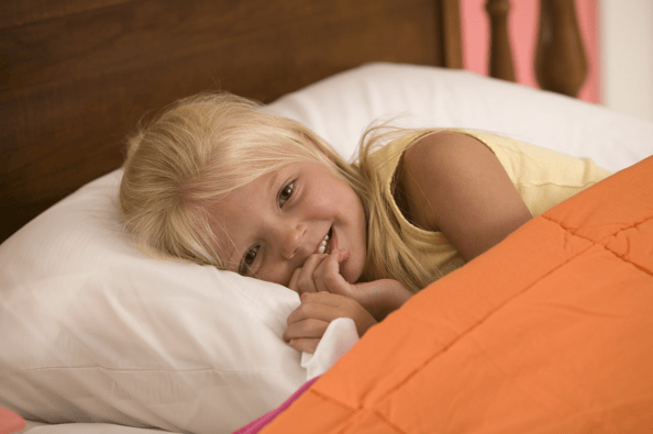 Child with yellow top laying in bed with an orange duvet cover