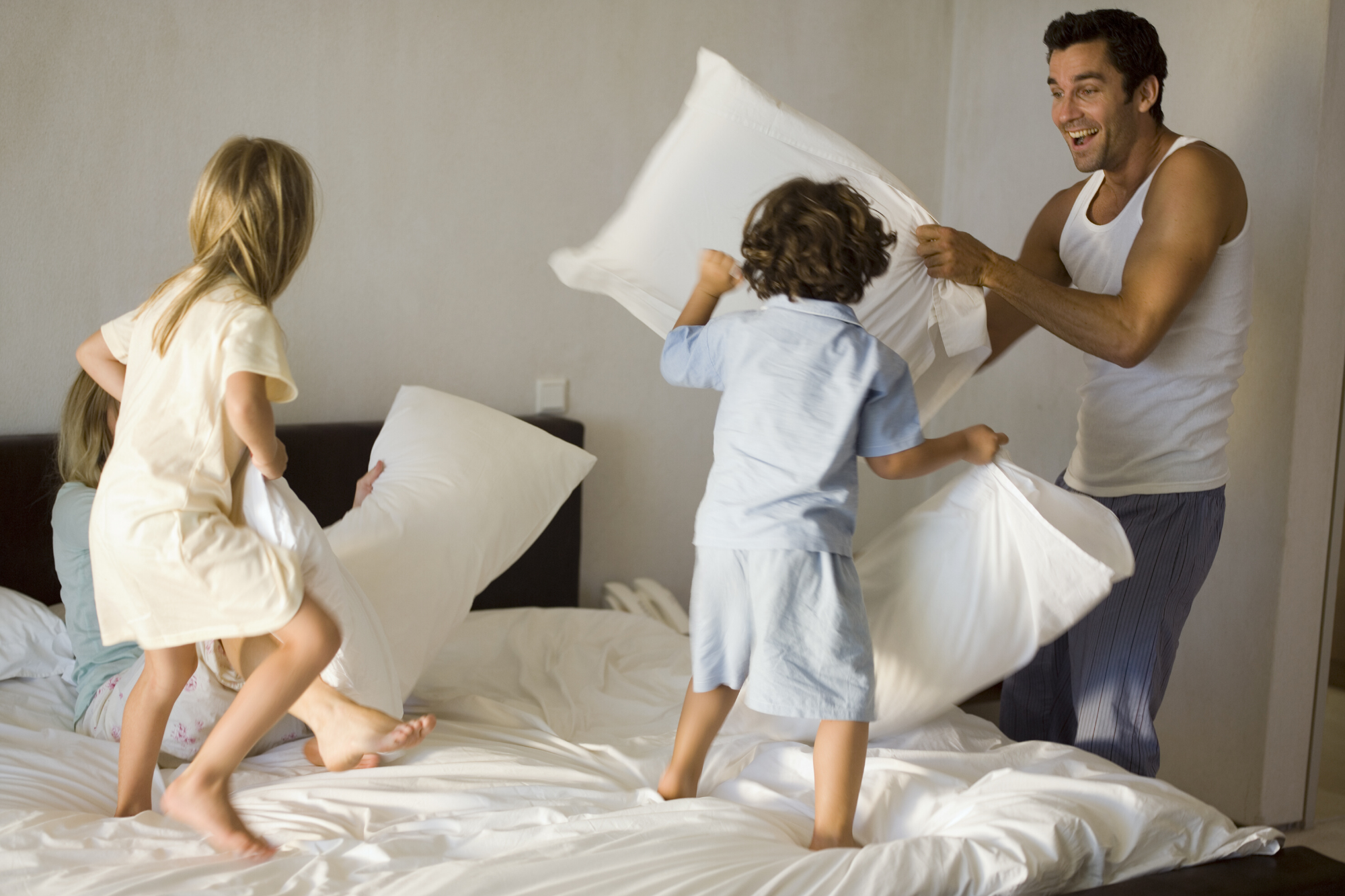 Dad having a pillow fight with his two toddlers in the bedroom