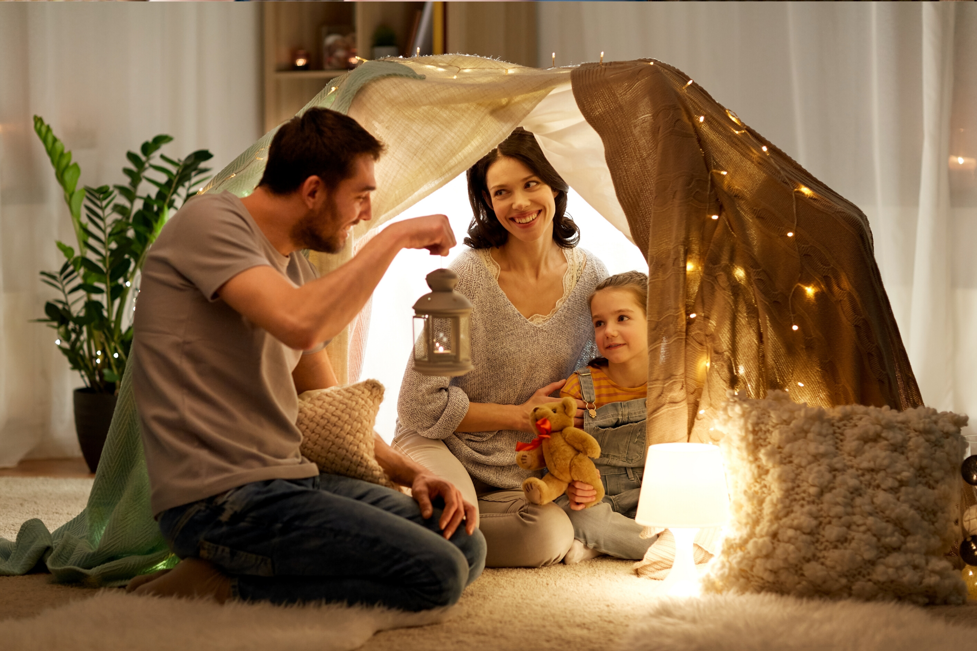 Mother and Father playing with their child in an indoor fabric lit up tent