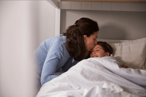Mother giving her child a kiss on her head before bedtime