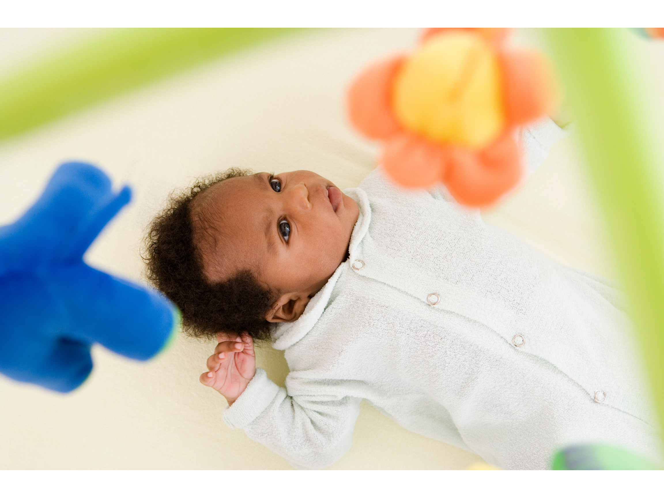 Newborn baby laying in his cot looking up at a toy mobile