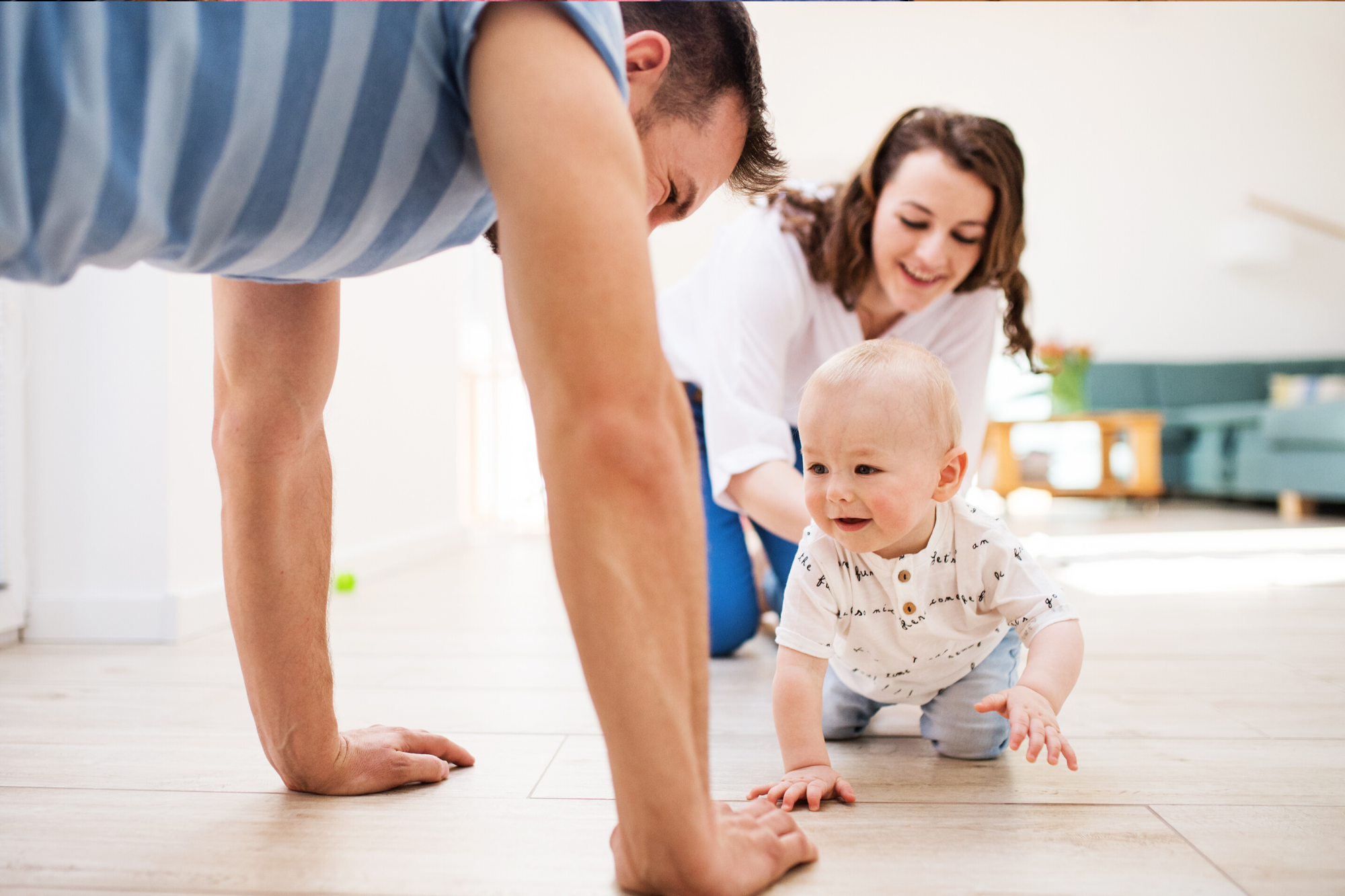 Blonde baby crawling towards his father, mother is behind him holding him steady