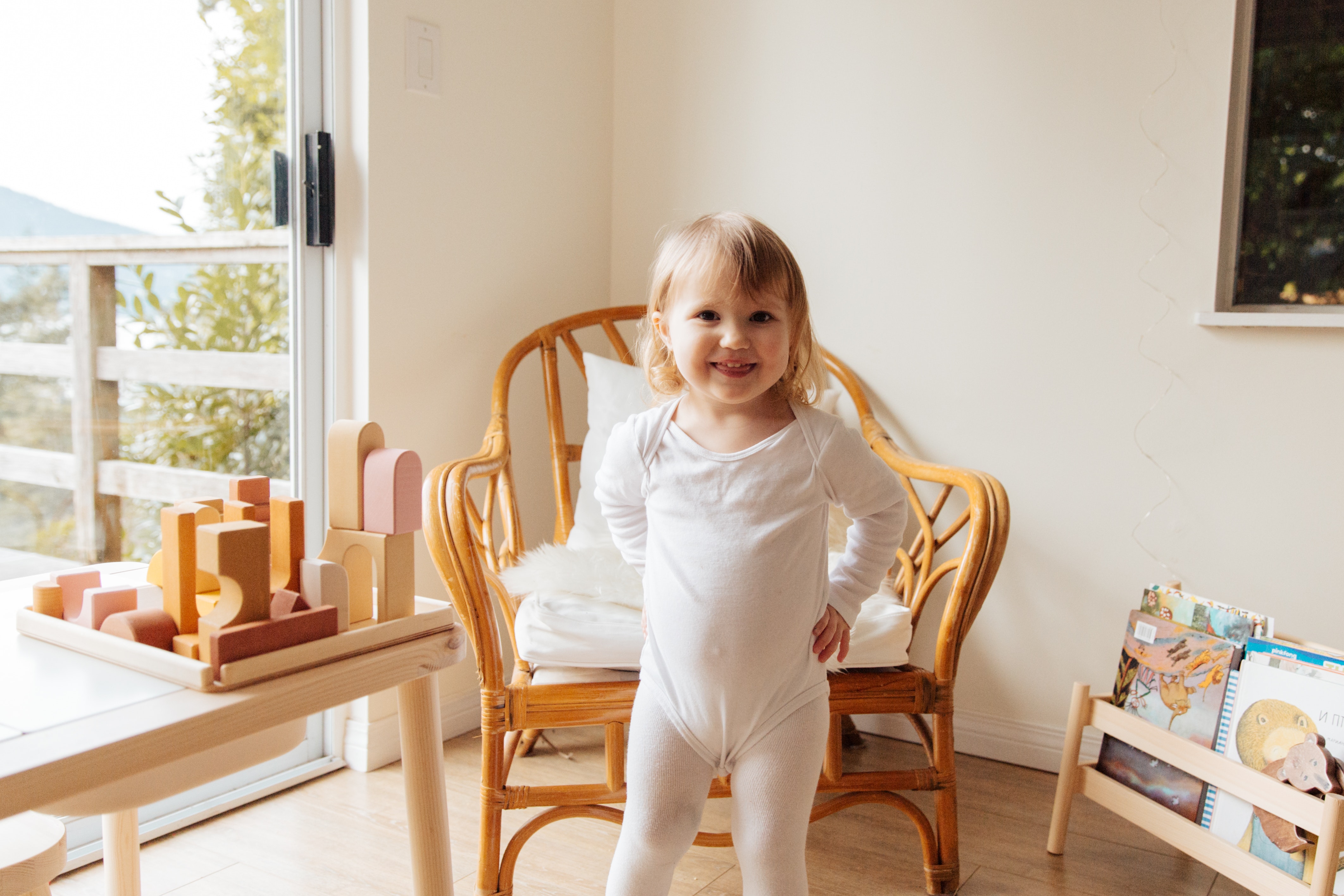 Girl in white onesie standing in front of a wooden chair