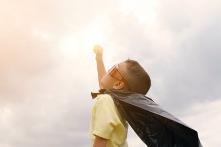 Toddler pointing to the sky, wearing a cape and sunglasses pretending to be a superhero