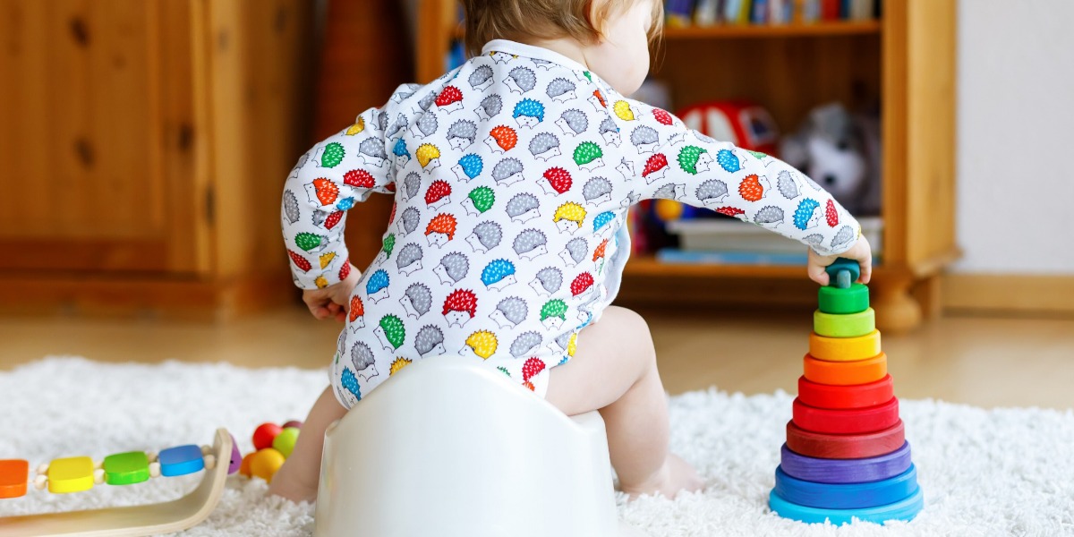 Child wearing a colourful bodysuit, potty training at home and playing with his multi-coloured stack toy