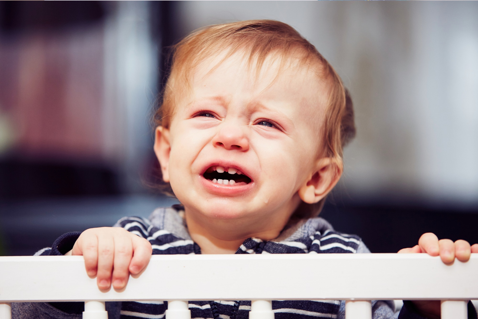 Baby boy crying while holding onto the edge of his cot