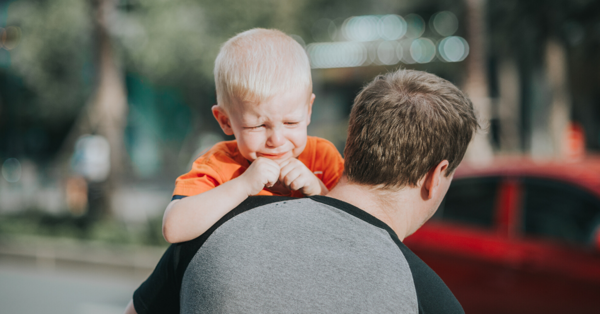 Child wearing an orange t-shirt crying while his dad holds him
