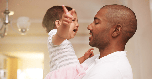 Dad wearing a white top holding his crying baby close to his face