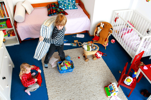 Toddler helping his little sister tidy up bedding and toys in their bedroom