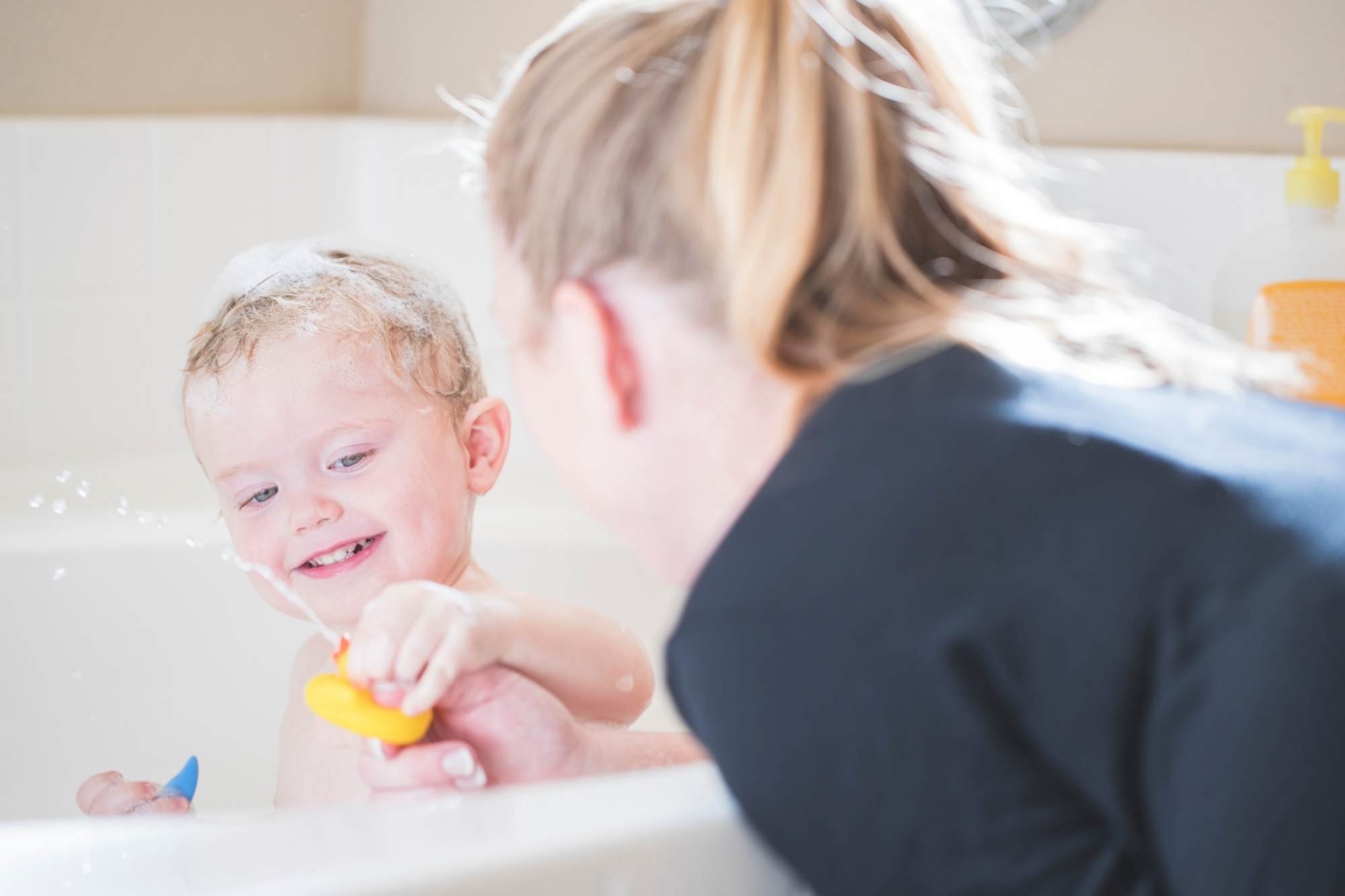 Mum playing with her preschooler and a rubber duck who is having a bath 