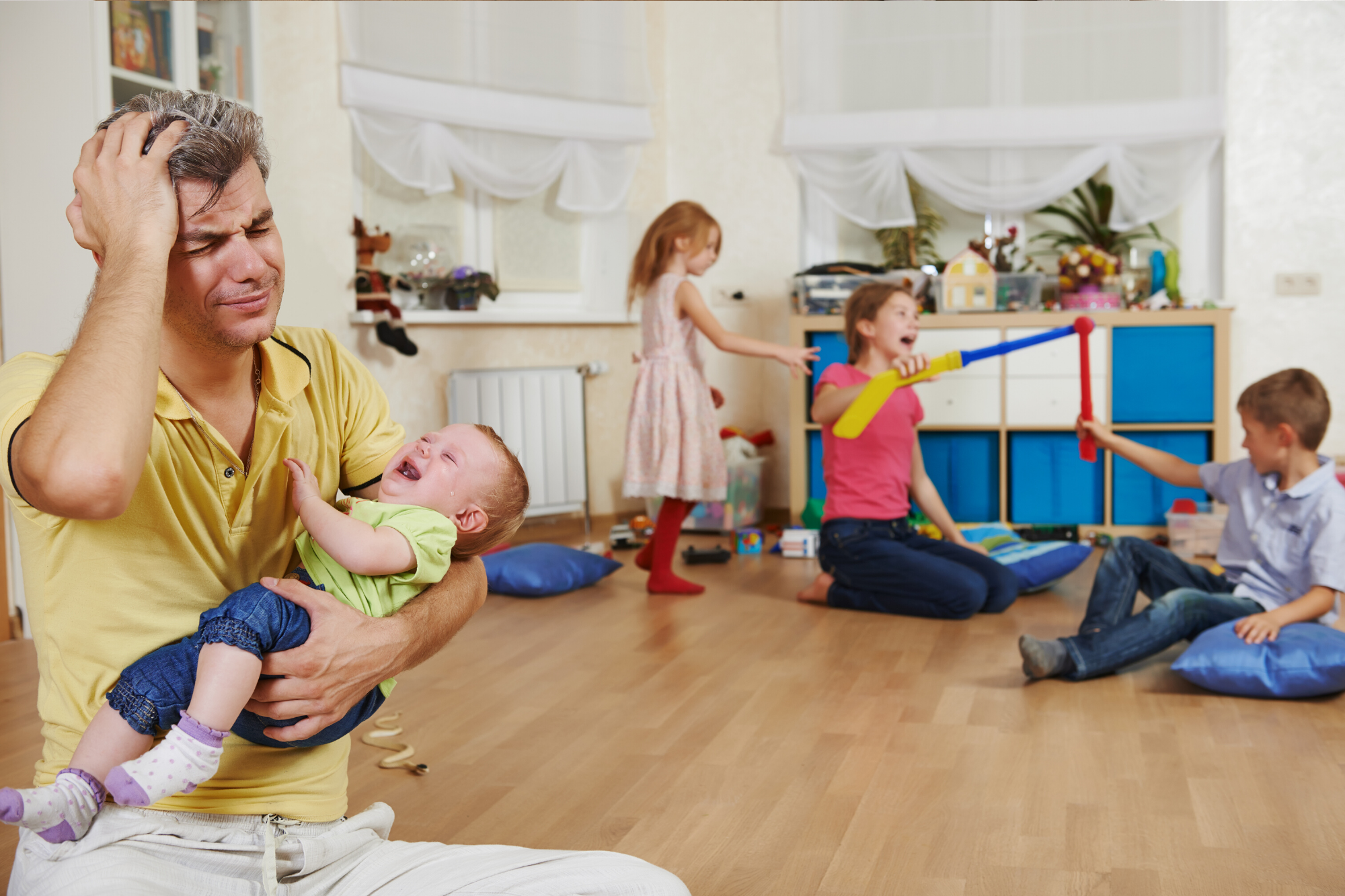 Father in a yellow top holding a crying baby while feeling overwhelmed