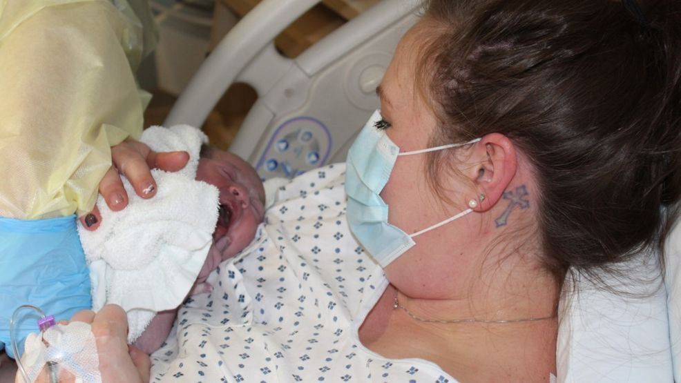 Mother wearing a face mask while holding her newborn baby during lockdown