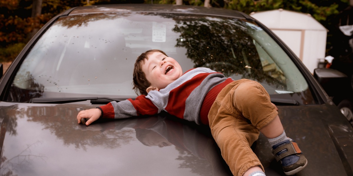 Toddler laying on the car bonnet waiting to start a road trip