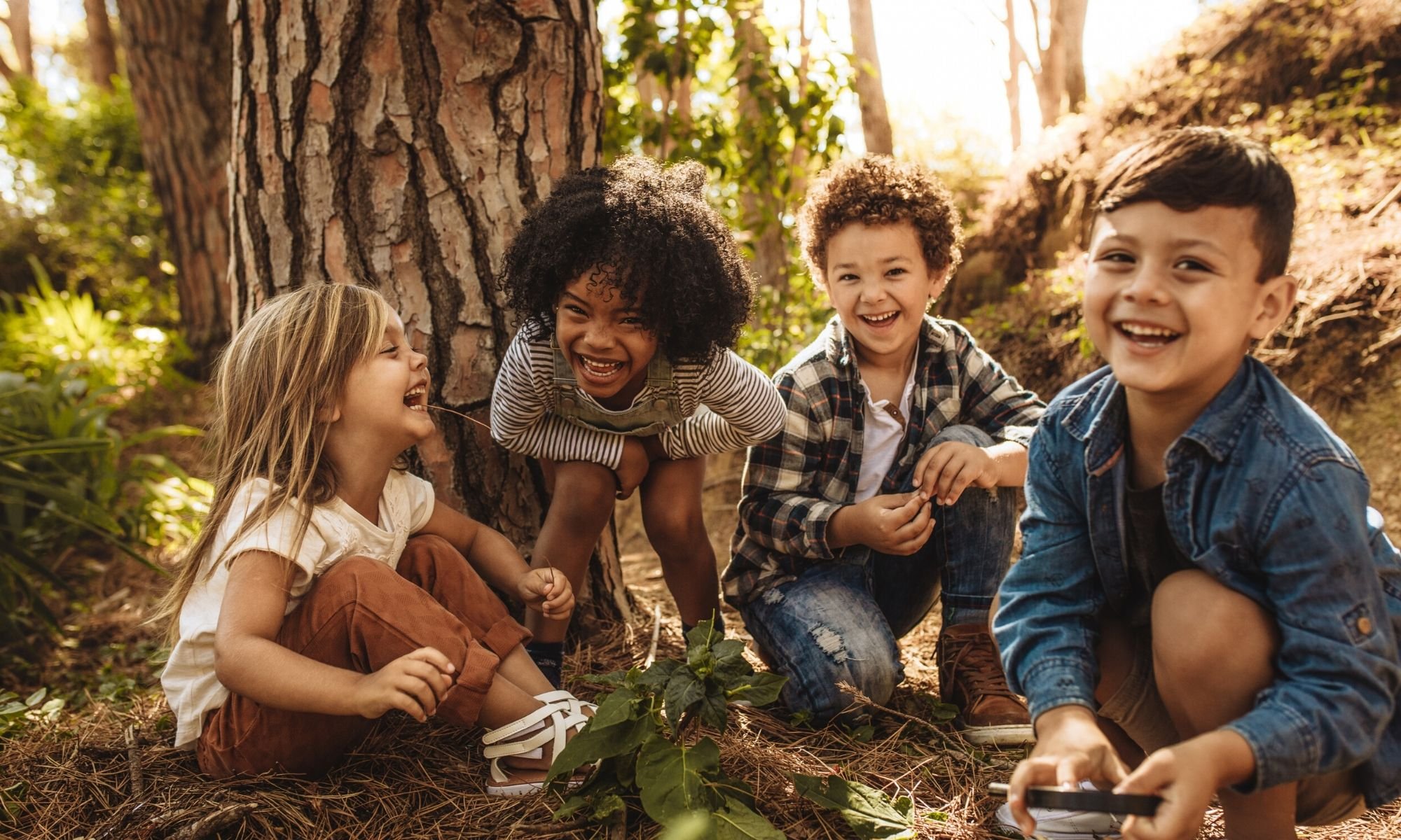 Toddlers of different races playing outdoors near a tree