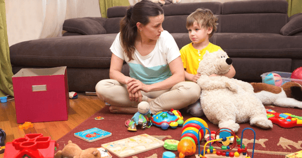 Stressed Mother sitting on the living room floor with her toddler surrounded by toys