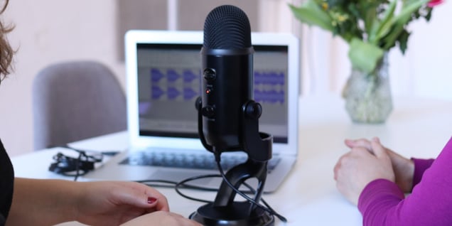 Two people sat at a table in front of a podcast recording microphone