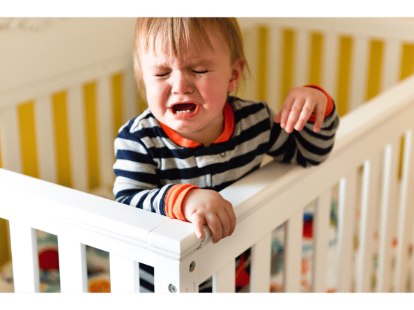 Toddler wearing a striped top having a tantrum while standing up in a cot