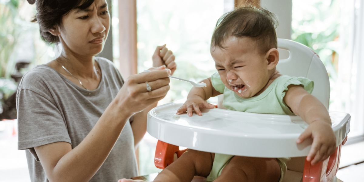 Mother struggling with her toddler throwing a tantrum during feeding time