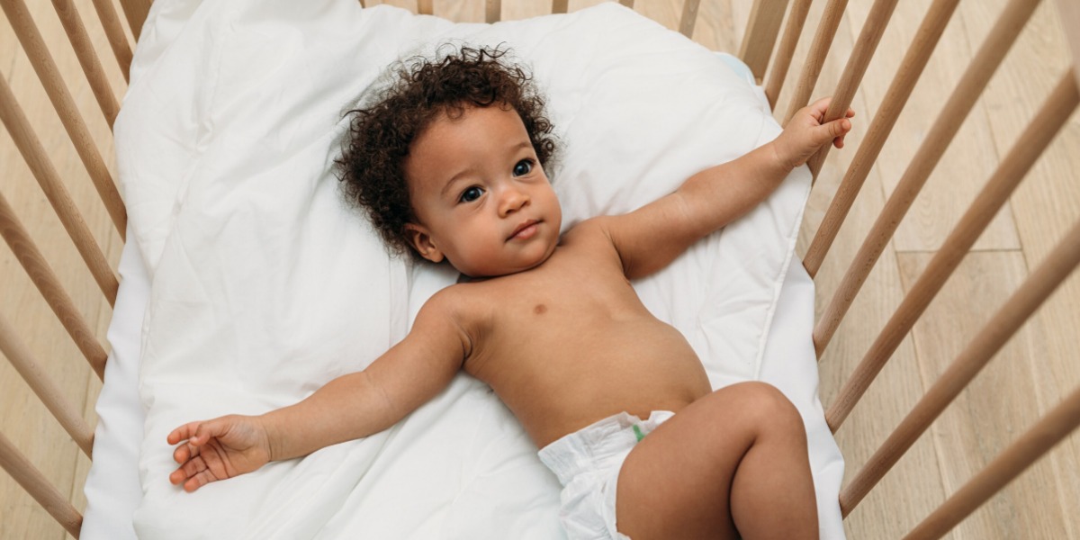 Baby wearing a nappy lying in a cot with their arms stretched out