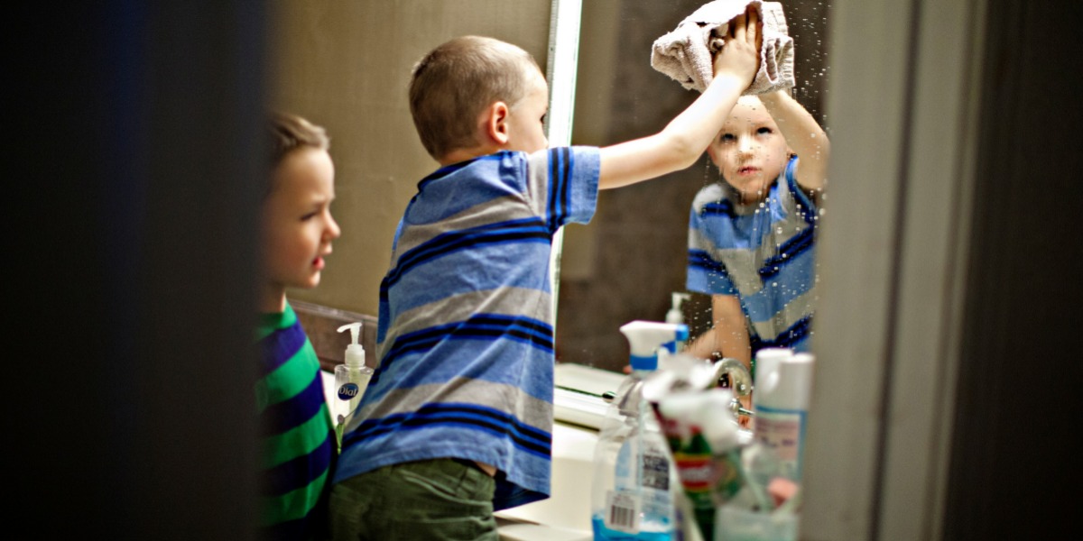 Two toddlers cleaning a bathroom mirror