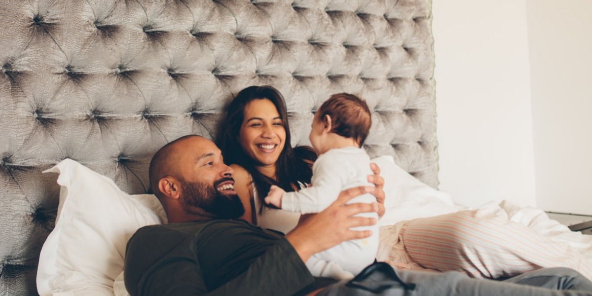 Two parents smiling in bed while holding their baby