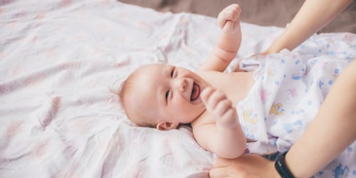 Baby laying down smiling, and raising their hands in happiness