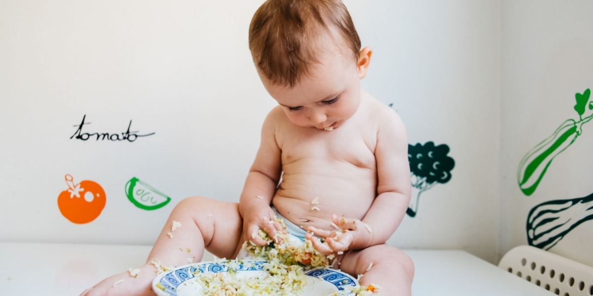 Toddler wearing a nappy sat playing with food in a bowl