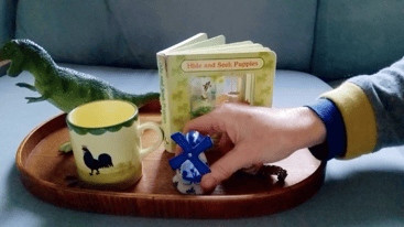 Nursery manager creating an activity with a ceramic windmill, book, mug and toy dinosaur