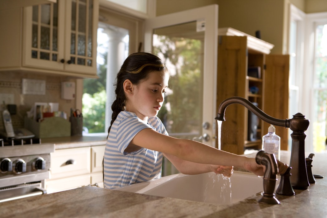 Young girl stood at the sink in her kitchen washing her hands 