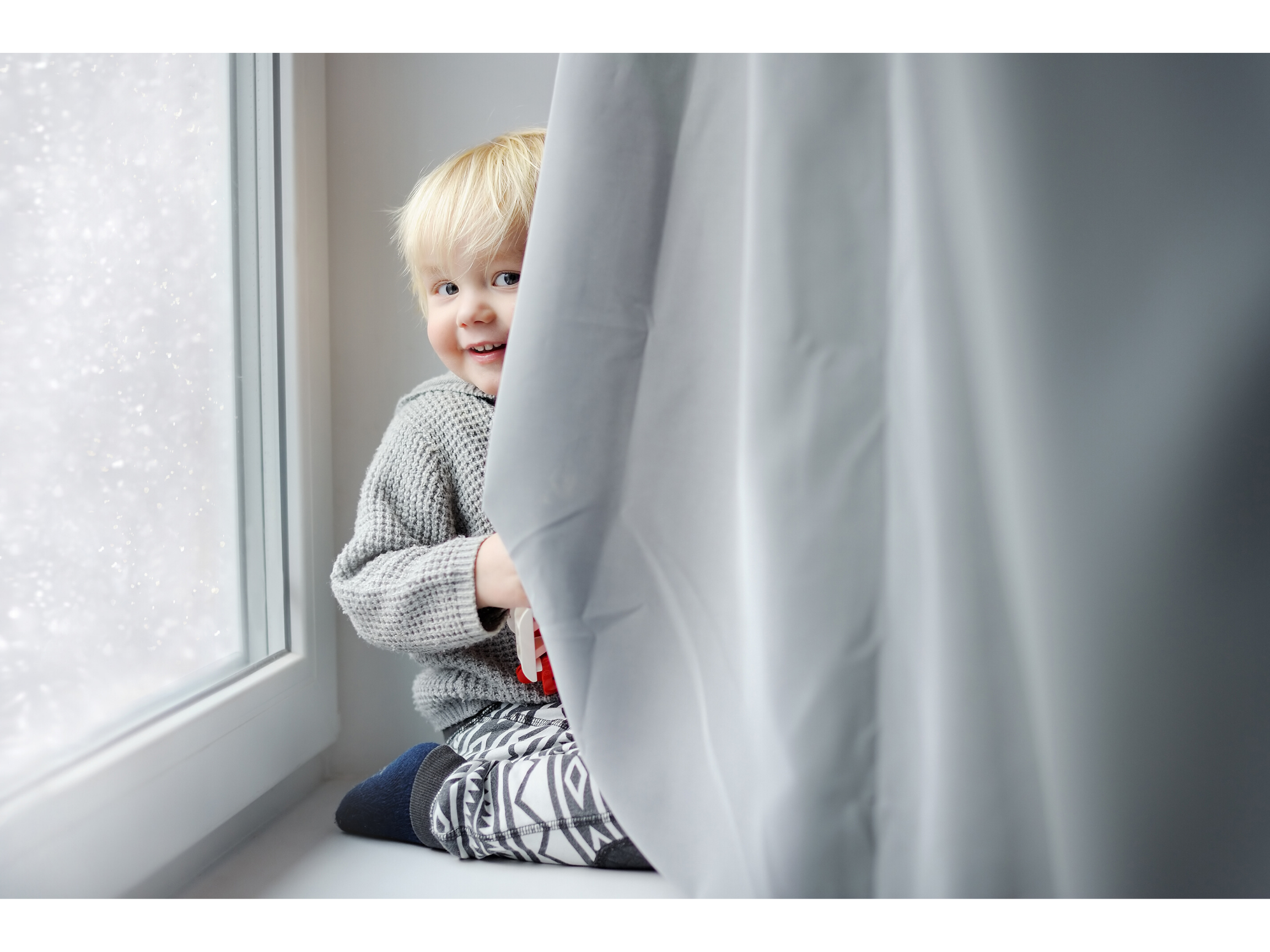 Blonde child playing behind a grey curtain preparing to return to his nursery during the COVID-19 pandemic