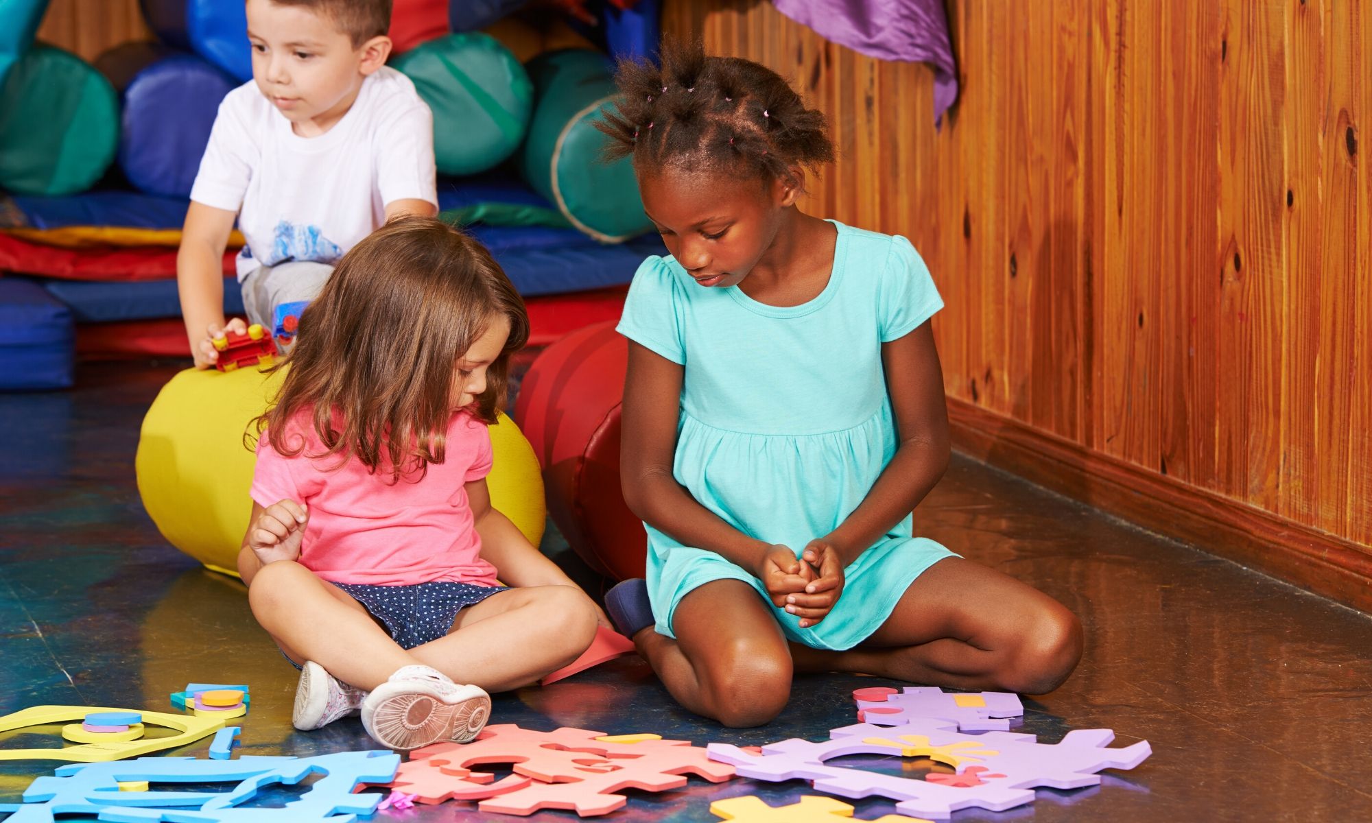 Children at their pre-school nursery sitting down to play with a colourful foam jigsaw puzzle
