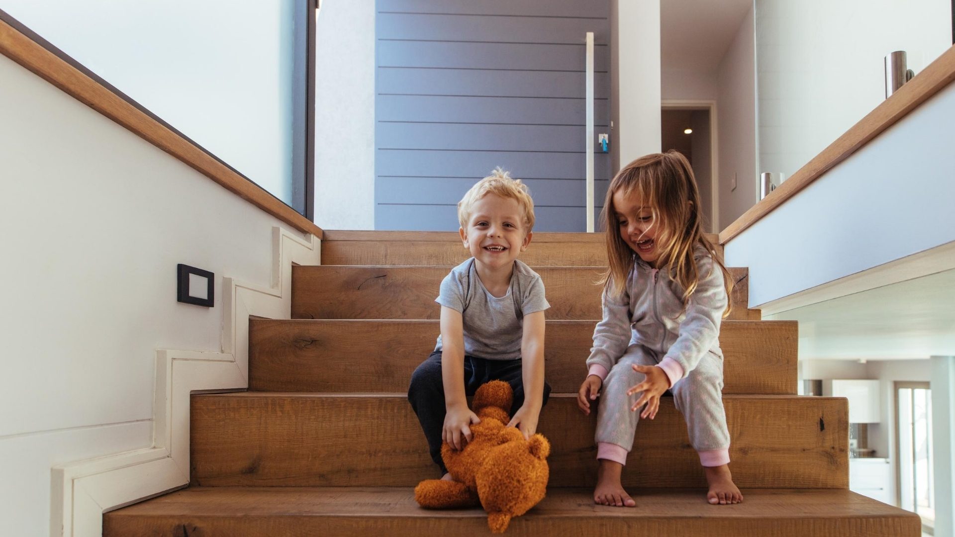 Children playing with a brown teddy bear on the stairs at home
