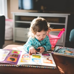 Toddler in a green long sleeve t-shirt pointing at the pictures in a book